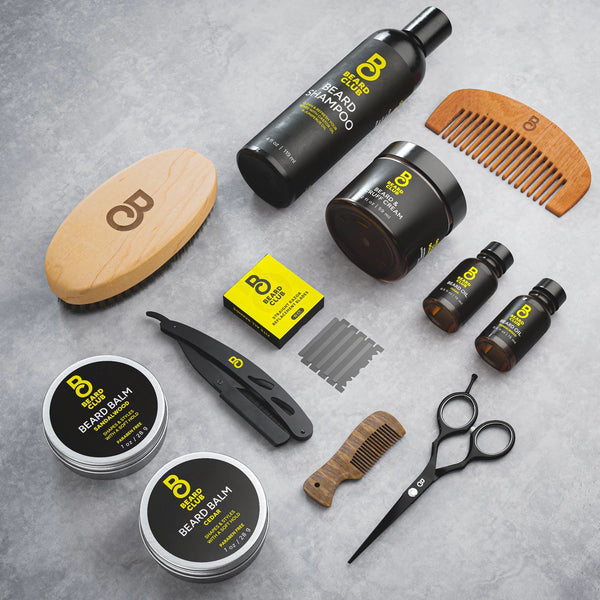 Beard Club grooming kit with shampoo, balm, oil, wooden combs, brush, and straight razor on a grey surface.